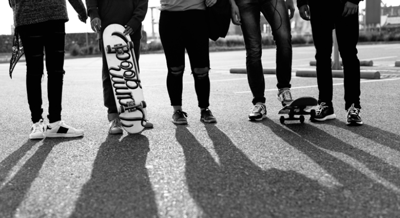 young people walking down the street holding a skateboard