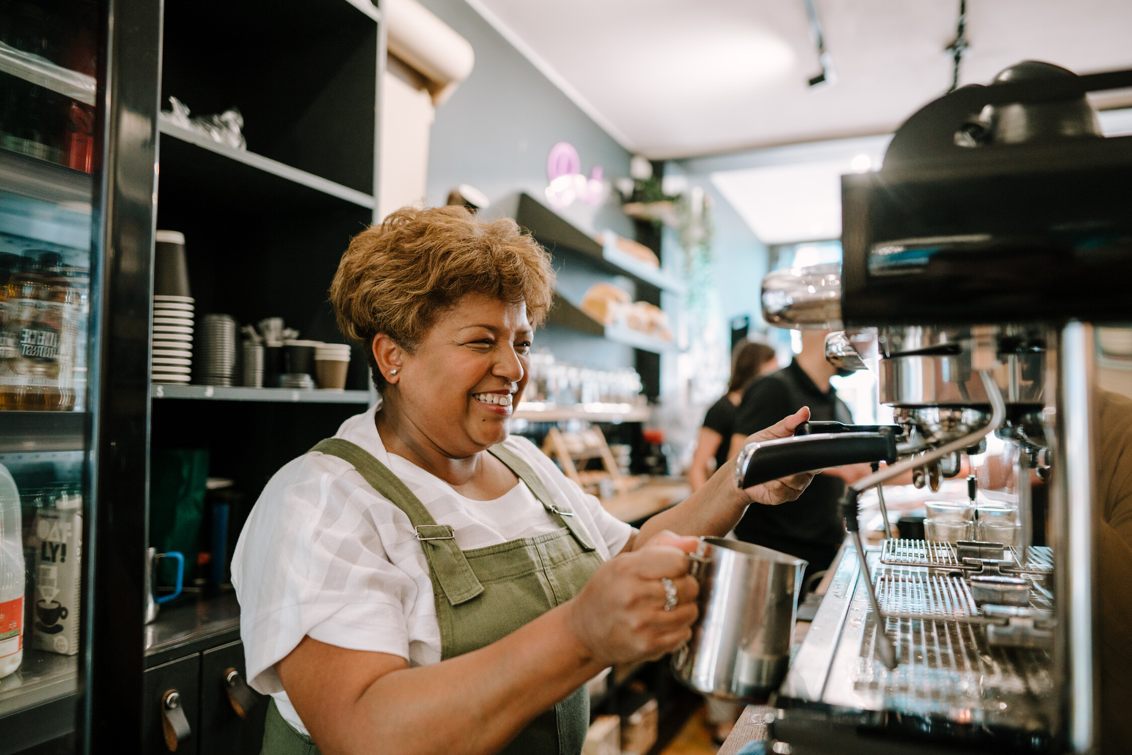 Woman is working in a coffee shop on a coffee machine smiling