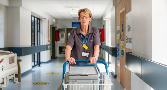 Volunteer pushing an empty trolley through a hospital corridor smiling