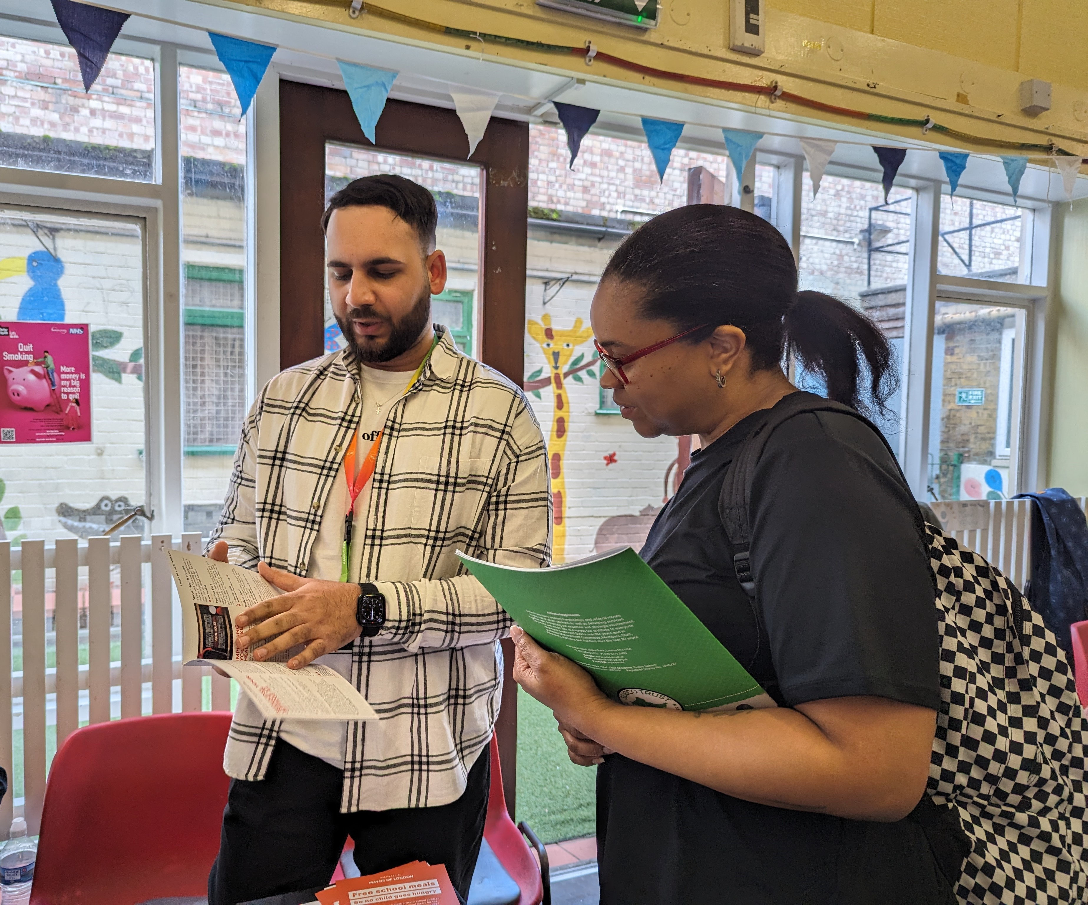 A Well Newham Hub Advisor holding 5 ways to a healthier life speaking to a resident