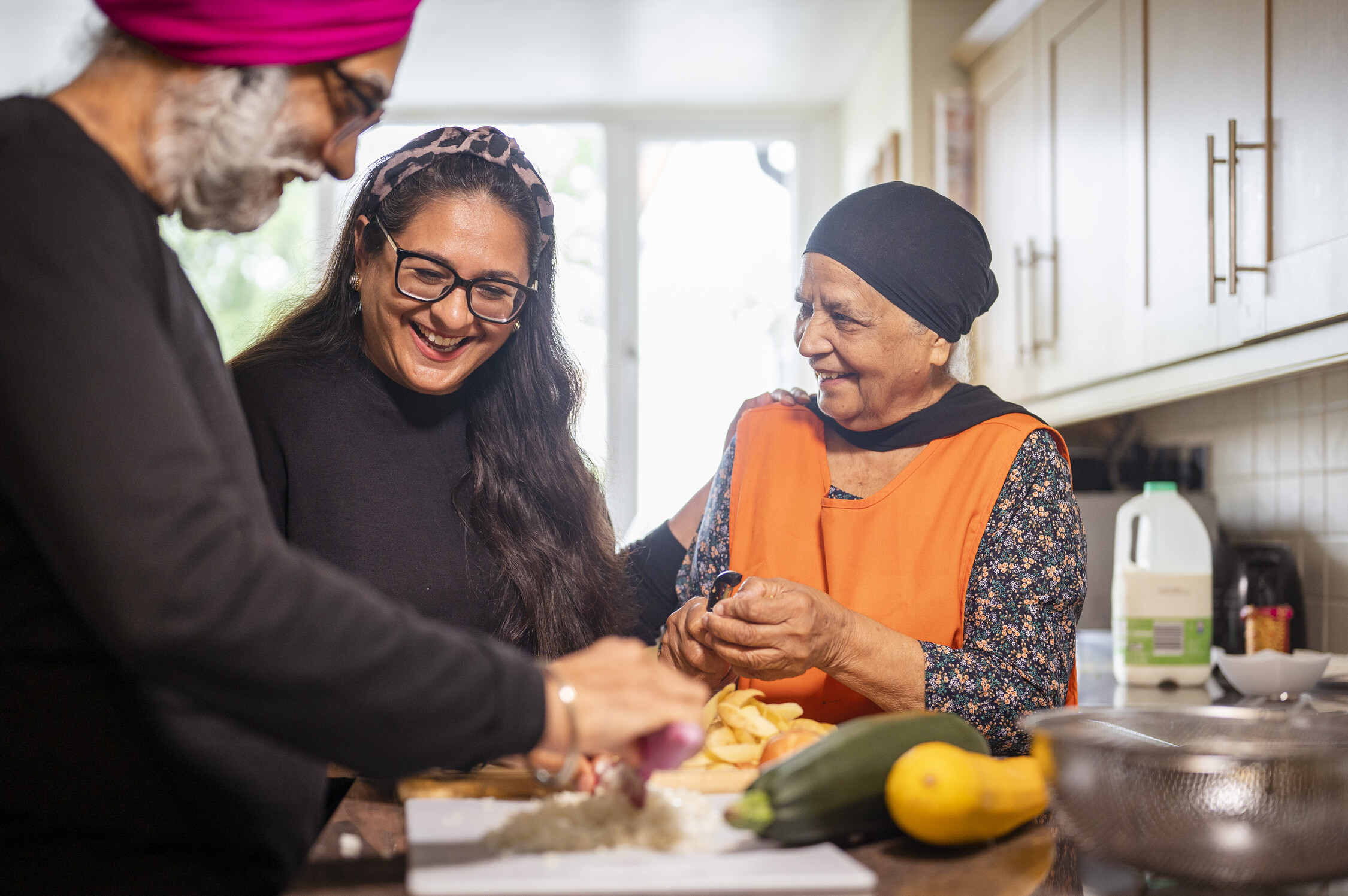 An older couple are cooking together with a younger lady who is helping them in the kitchen