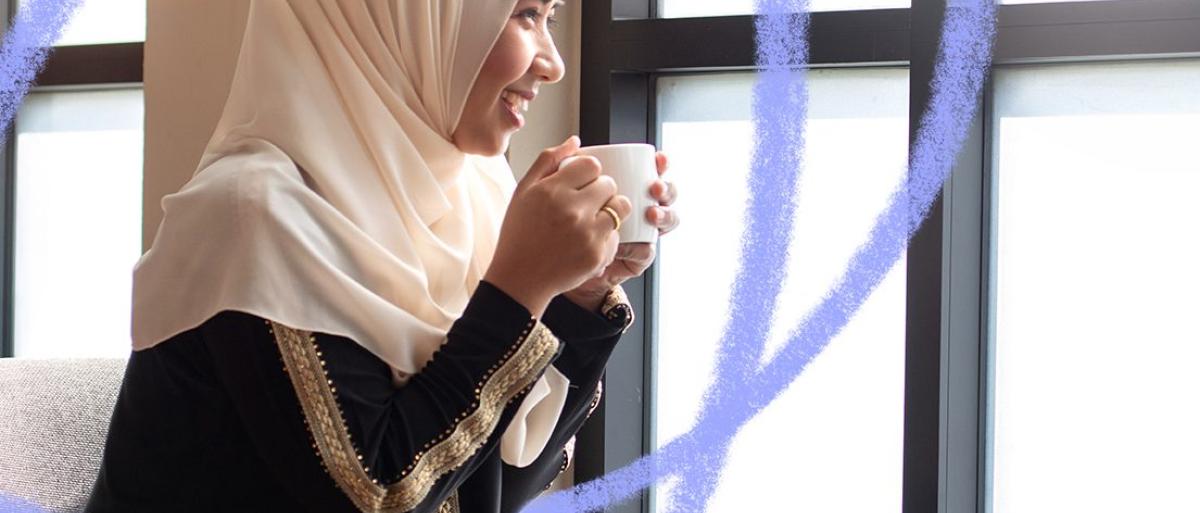 woman wearing a headscarf drinking from a mug and smiling