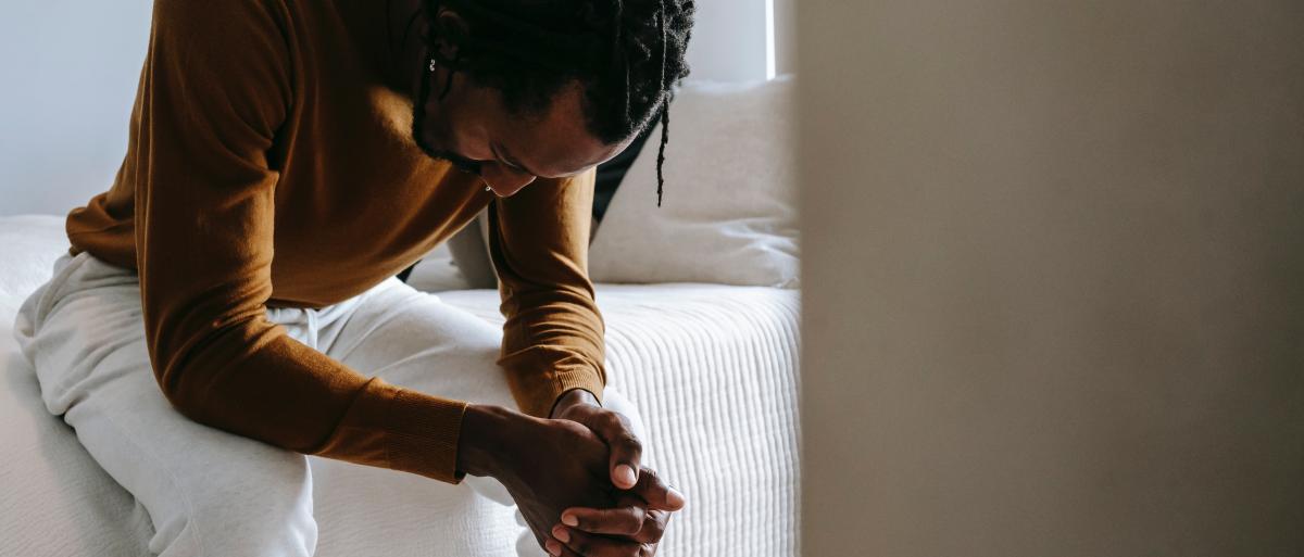 Man sat on the edge of a bed looking sad