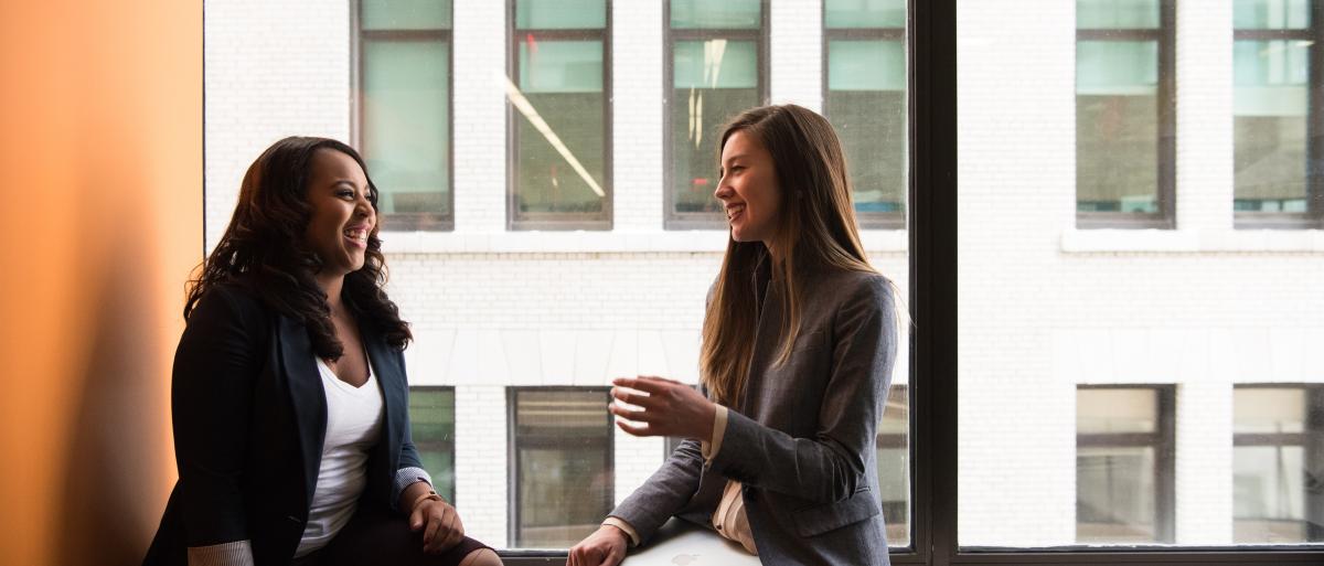 Two women talking in front of a window