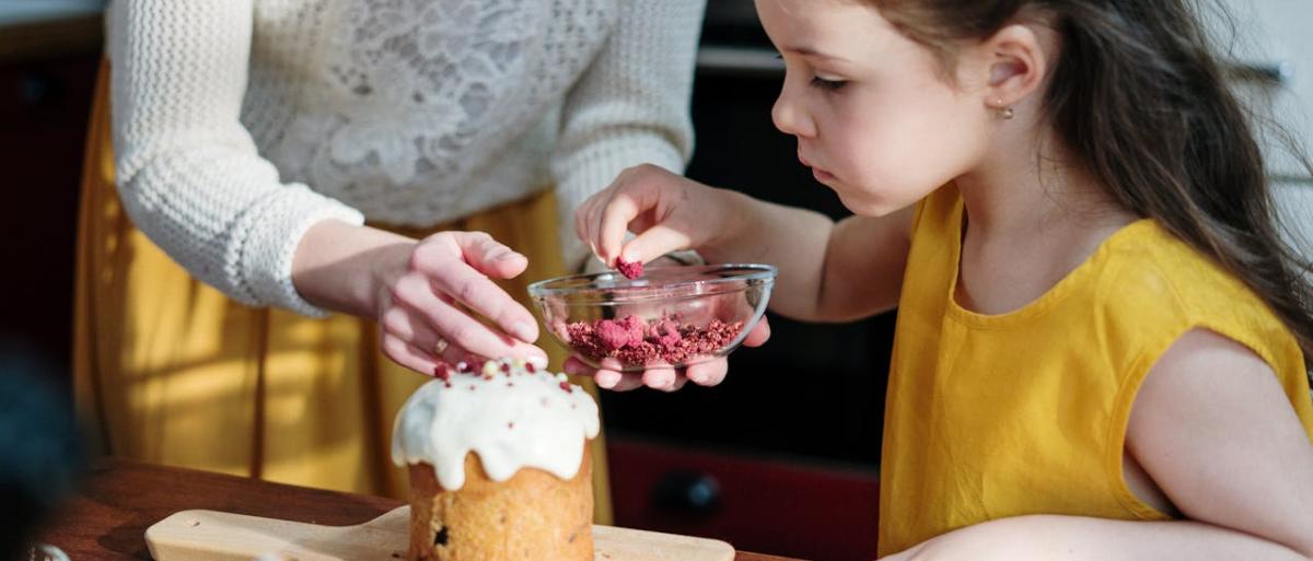 A little girl adding sprinkles to a cake
