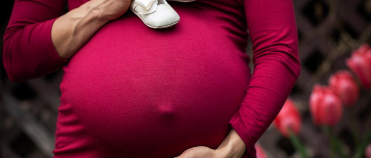 A pregnant woman holding baby shoes and her bump