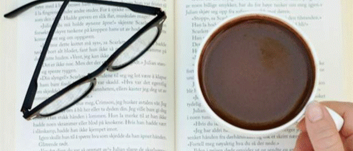 Someone holding a cup of tea with a reading glass and a book