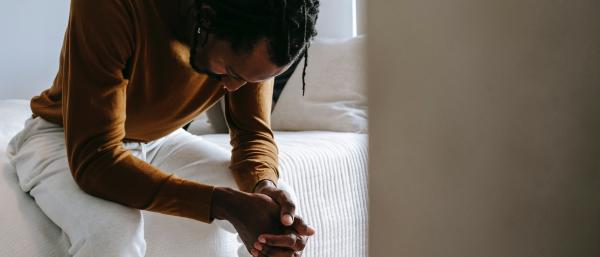Man sat on the edge of a bed looking sad