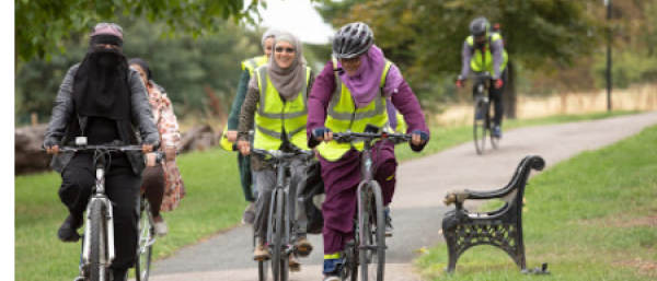 Muslim women cycling together through a park