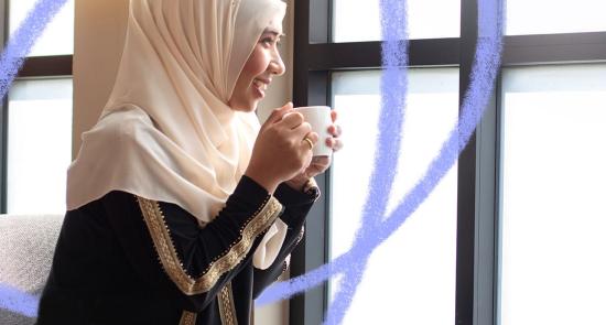 woman wearing a headscarf drinking from a mug and smiling