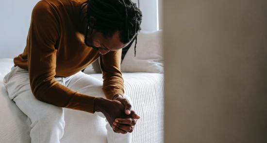 Man sat on the edge of a bed looking sad