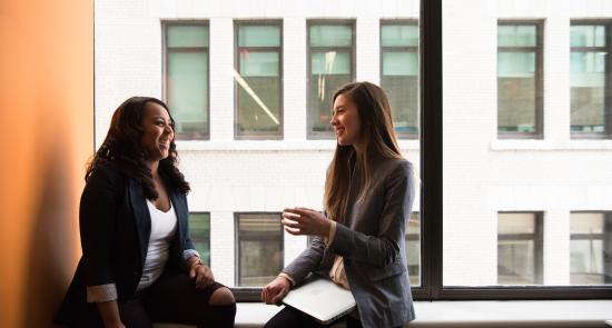 Two women talking in front of a window