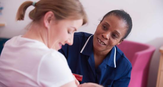 Nurse is talking to a new mum feeding her baby