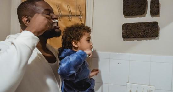 Dad helping his son to brush his teeth in front of a mirror