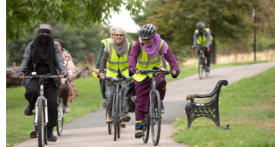 Muslim women cycling together through a park