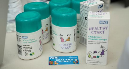 Table with bottles of healthy start vitamins on top. The bottles are white with a turquoise cap.
