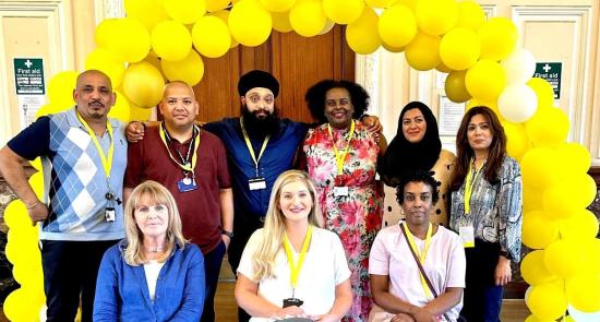 Photo of the Community Neighbourhood Link Workers team sat together in a hall in front of a yellow balloon arch