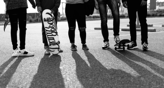 young people walking down the street holding a skateboard