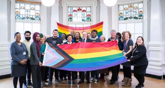 Colleagues holding up the LGBTQIA+ flag as part of LGBT+ History Month events