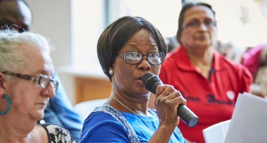 An older woman with a microphone sharing her opinions at the reference group