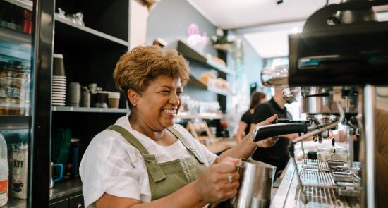 Woman is working in a coffee shop on a coffee machine smiling