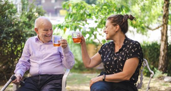 Man sat with his carer in the garden drinking tea