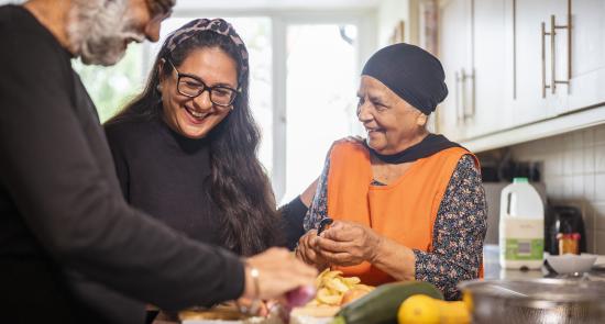 An older couple are cooking together with a younger lady who is helping them in the kitchen